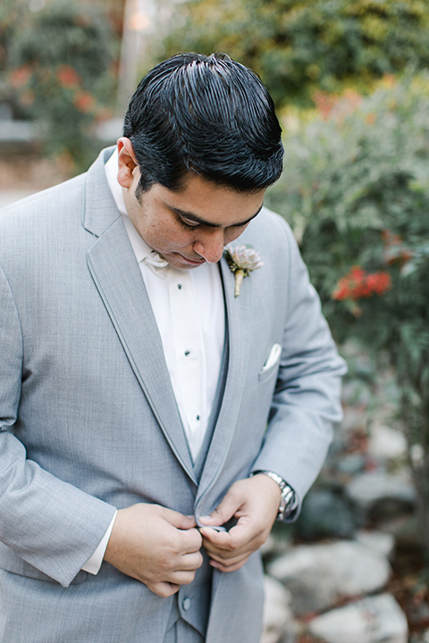 hidden-acres-wedding-groom-buttoning-jacket-groom-in-grey-suit-with-white-bow-tie