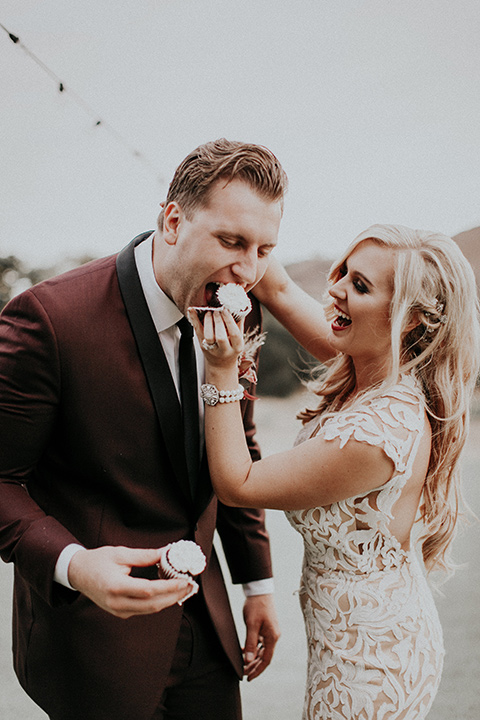 orange-county-vow-bride-feeding-groom-bride-in-a-lace-modern-fitted-gown-with-a-nude-underlay-groom-in-a-burgundy-tuxedo-with-a-black-shawl-lapel