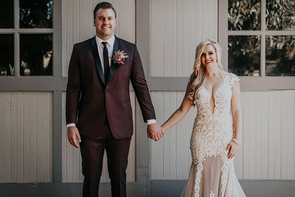 orange-county-vow-renewal-bride-and-groom-smiling-looking-at-camera-bride-in-a-lace-modern-fitted-gown-with-a-nude-underlay-groom-in-a-burgundy-tuxedo-with-a-black-shawl-lapel