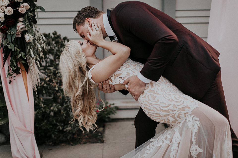 orange-county-vow-renewal-first-kiss-bride-in-a-lace-modern-fitted-gown-with-a-nude-underlay-groom-in-a-burgundy-tuxedo-with-a-black-shawl-lapel