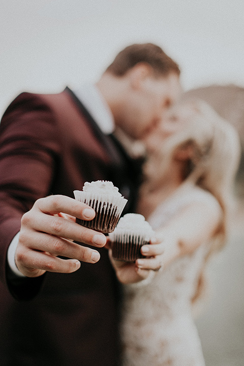 orange-county-vow-renewal-holding-cupcakes-bride-in-a-lace-modern-fitted-gown-with-a-nude-underlay-groom-in-a-burgundy-tuxedo-with-a-black-shawl-lapel