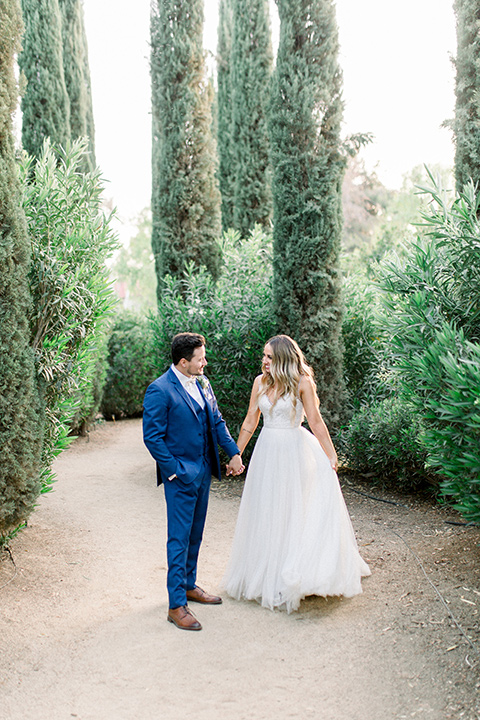  bride in a white a line gown with straps and a big white and sage floral bouquet and cathedral length veil, the groom in a dark blue suit with a white bow tie