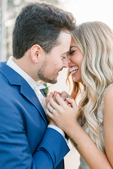  bride in a white a line gown with straps and a big white and sage floral bouquet and cathedral length veil, the groom in a dark blue suit with a white bow tie 