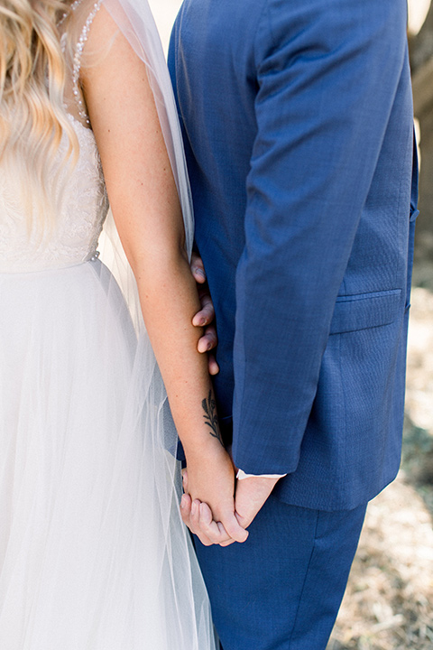  bride in a white a line gown with straps and a big white and sage floral bouquet and cathedral length veil, the groom in a dark blue suit with a white bow tie