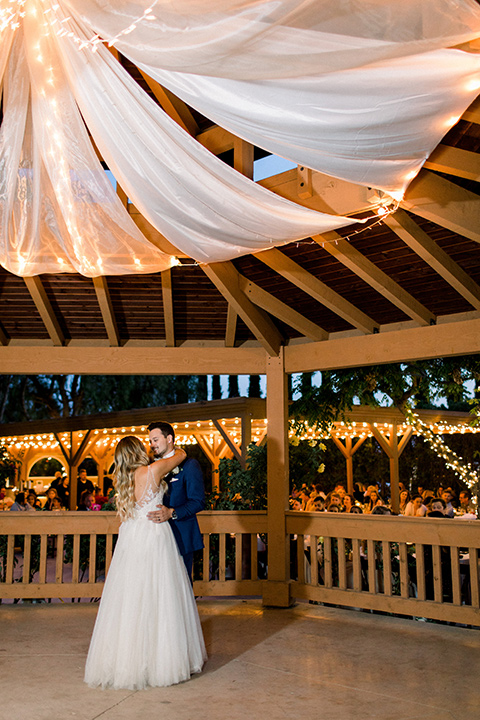  bride in a white a line gown with straps and a big white and sage floral bouquet and cathedral length veil, the groom in a dark blue suit with a white bow tie 