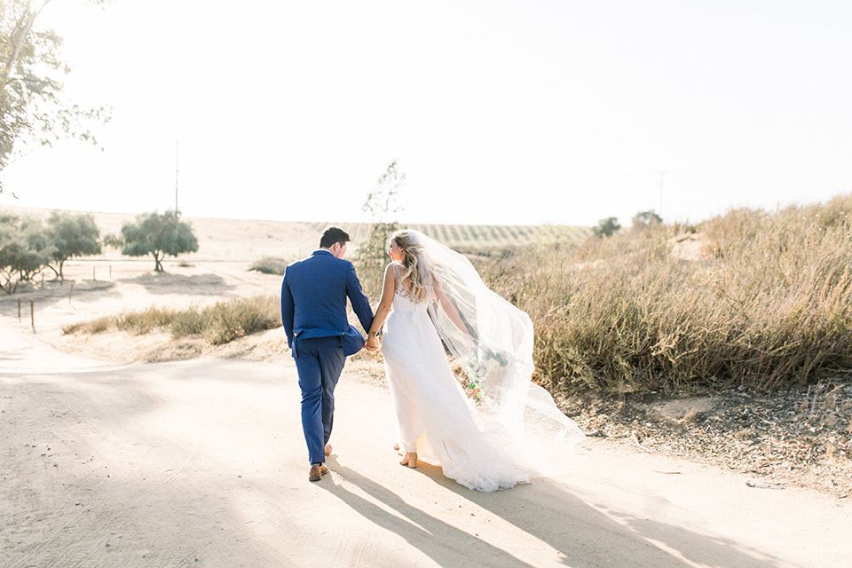  bride in a white a line gown with straps and a big white and sage floral bouquet and cathedral length veil, the groom in a dark blue suit with a white bow tie 