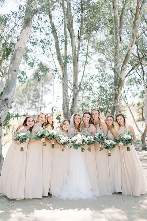  bride in a white a line gown with straps and a big white and sage floral bouquet and cathedral length veil, bridesmaids in neutral long gowns