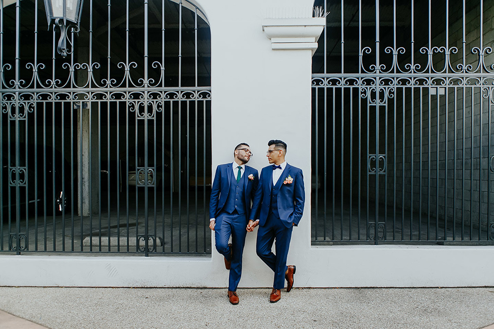 loquita-shoot-grooms-against-wall-looking-at-each-other-grooms-in-cobalt-blue-suits-with-one-with-a-green-tie-and-the-other-with-a-blue-bow