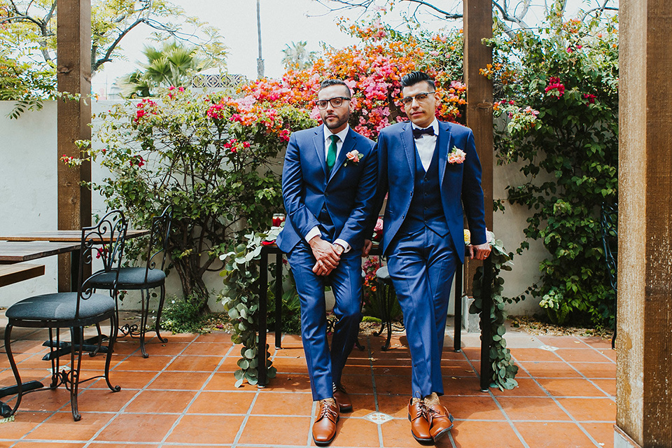 loquita-shoot-grooms-outside-sitting-on-table-grooms-in-cobalt-blue-suits-with-one-with-a-green-tie-and-the-other-with-a-blue-bow