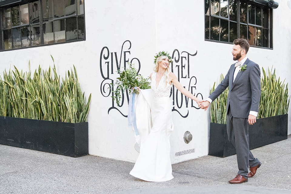 luce-loft-bride-and-groom-walking-outside-bride-in-a-fit-and-flare-gown-with-straps-groom-in-a-charcoal-suit-with-champagne-bow-tie