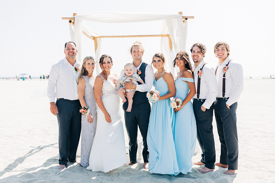 San-Diego-Beach-wedding-bridal-party-smiling-bridesmaids-in-bright-blue-dresses-groomsmen-in-suit-pants-and-suspenders-bride-ina-lace-formitting-dress-with-strapsand-a-veil-groom-in-a-suit-pants-and-vest