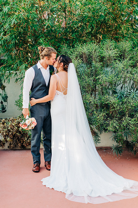 San-Diego-Beach-wedding-bride-and-groom-kissing-bride-in-a-lace-form-fitting-dress-with-straps-groom-in-a-casual-look-with-vest-and-pants-in-a-grey-suit-color