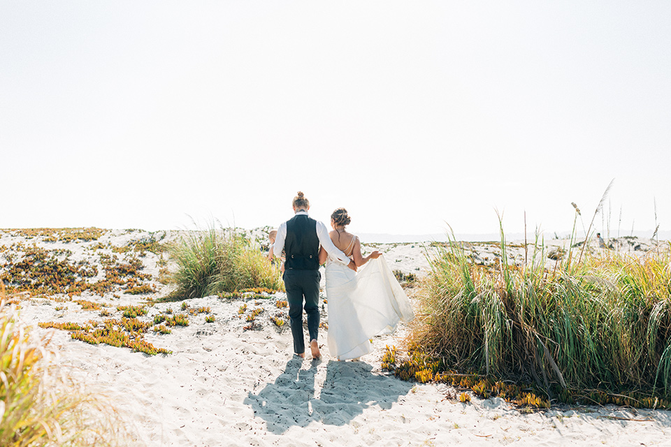 San-Diego-Beach-wedding-bride-and-groom-on-sand-bridesmaids-in-bright-blue-dresses-groomsmen-in-suit-pants-and-suspenders-bride-ina-lace-formitting-dress-with-strapsand-a-veil-groom-in-a-suit-pants-and-vest