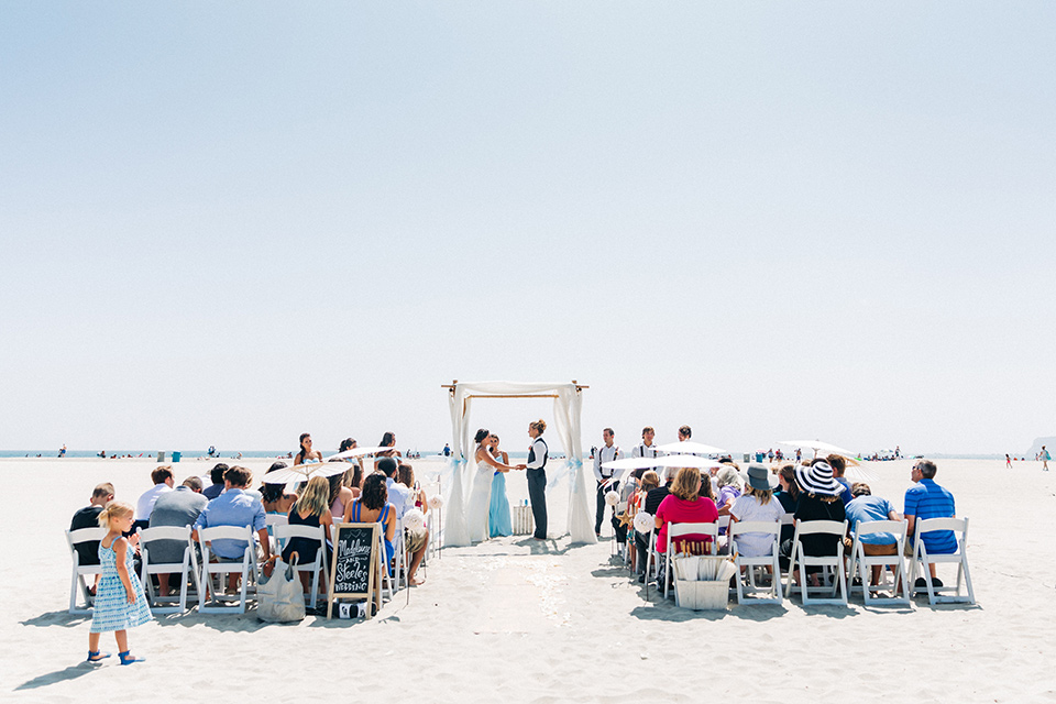 San-Diego-Beach-wedding-ceremony-bridesmaids-in-bright-blue-dresses-groomsmen-in-suit-pants-and-suspenders-bride-ina-lace-formitting-dress-with-strapsand-a-veil-groom-in-a-suit-pants-and-vest