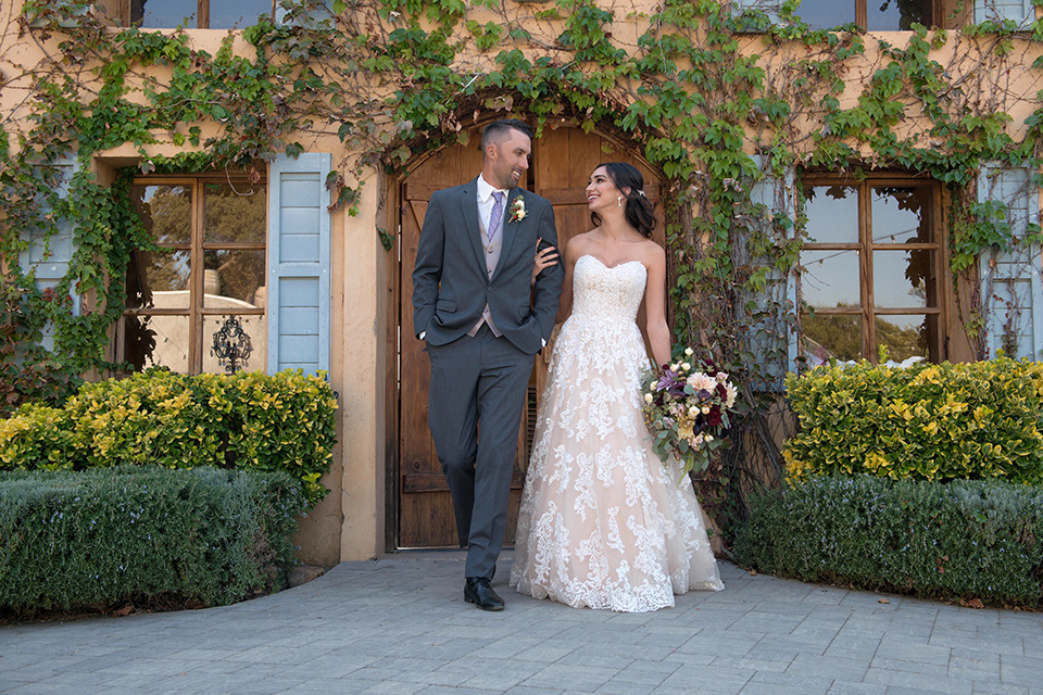 milagro-farms-shoot-bride-and-groom-walking-bride-in-a-fitted-lace-dress-groom-in-charcoal-suit-with-purple-tie