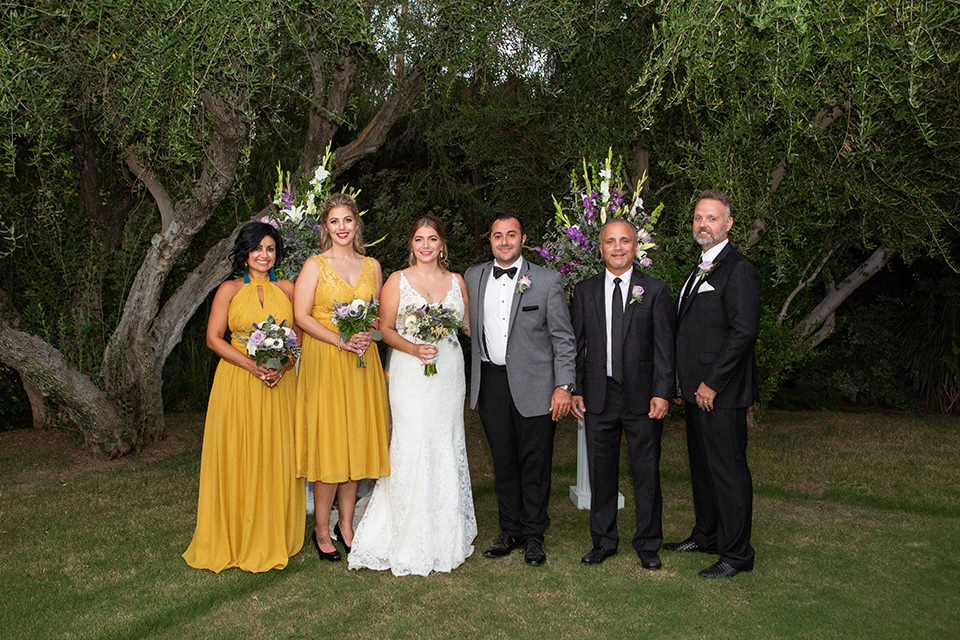 Palm-Springs-wedding-at-the-parker-bridal-party-outside-bridesmaids-in-mustard-yellow-dresses-groomsmen-in-black-tuxedos-bride-in-a-flowing-gown-with-straps-and-a-plunging-deep-v-neckline-groom-in-a-grey-tuxedo-with-black-trim-and-black-pants