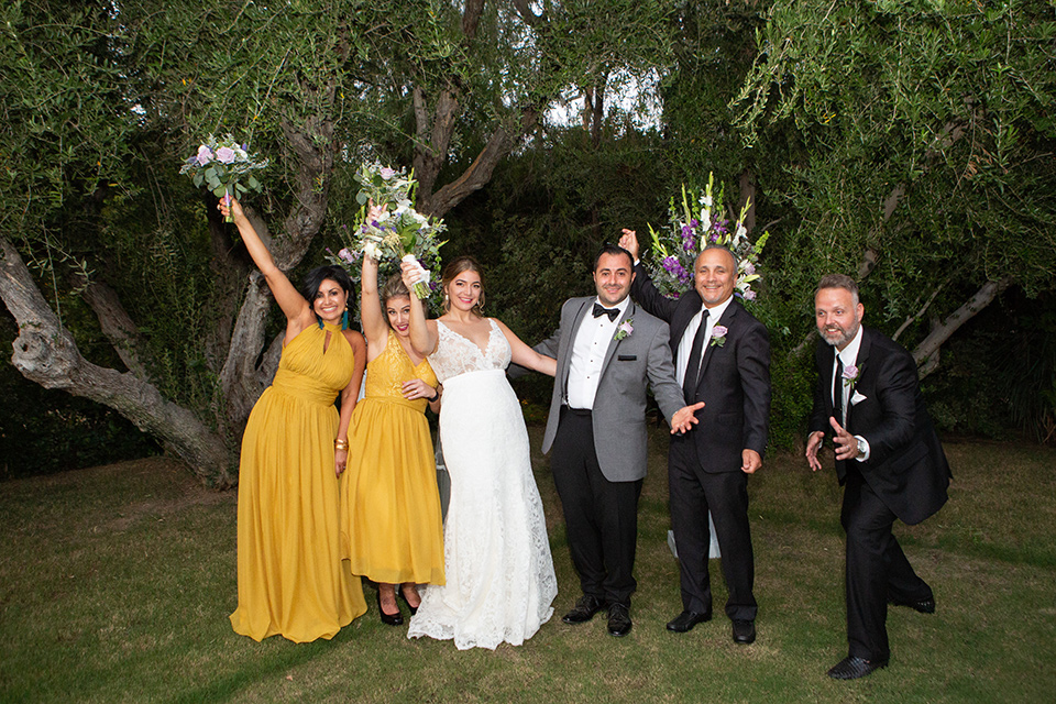 Palm-Springs-wedding-at-the-parker-bridal-party-bridesmaids-in-mustard-yellow-dresses-groomsmen-in-black-tuxedos-bride-in-a-flowing-gown-with-straps-and-a-plunging-deep-v-neckline-groom-in-a-grey-tuxedo-with-black-trim-and-black-pants