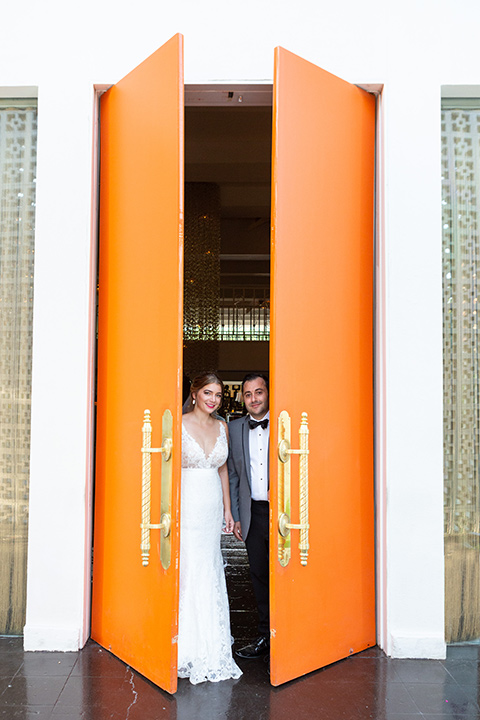 Palm-Springs-wedding-at-the-parker-bride-and-groom-peeping-out-the-orange-doors-bride-in-a-flowing-gown-and-a-deep-v-neckline-groom-in-grey-tuxedo-with-black-trim