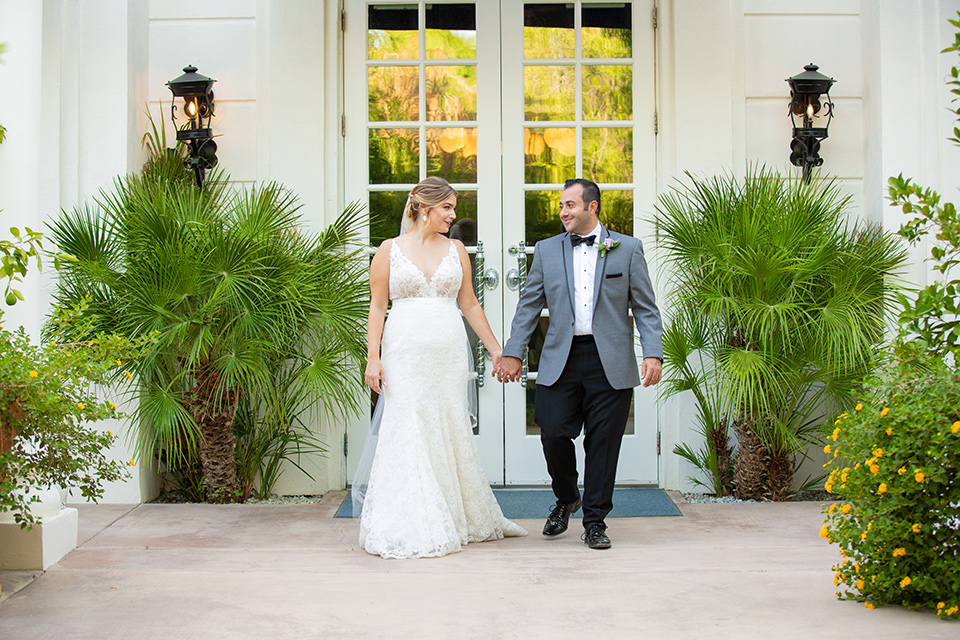 Palm-Springs-wedding-at-the-parker-bride-and-groom-walking-bride-in-a-flowing-gown-with-straps-and-a-plunging-deep-v-neckline-groom-in-a-grey-tuxedo-with-black-trim-and-black-pants