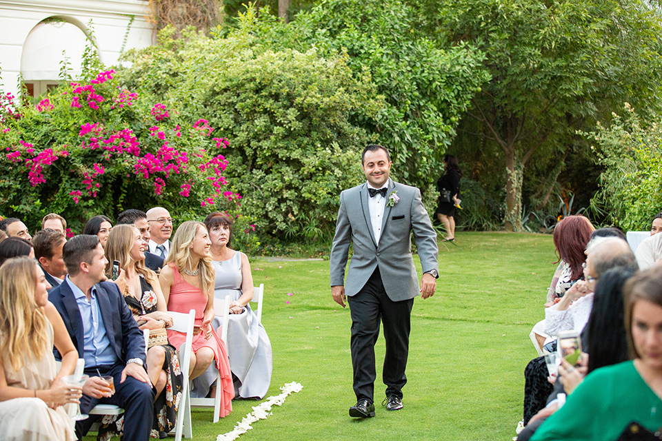 Palm-Springs-wedding-groom-walking-down-aisle-in-a-grey-tuxedo-with-black-trim-and-black-pants