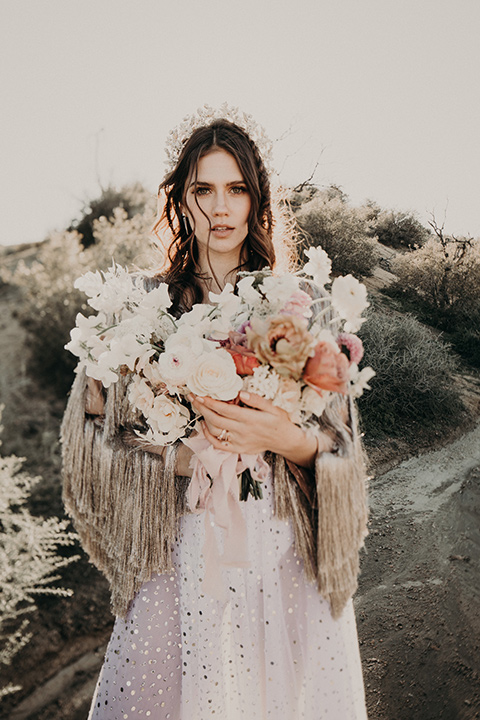 Rim-Rock-Ranch-Shoot-bride-alone-looing-at-camera-with-flowers-bride-wearing-a-sheer-gown-with-crystals-in-it-with-flutter-sleeves-and-a-crown