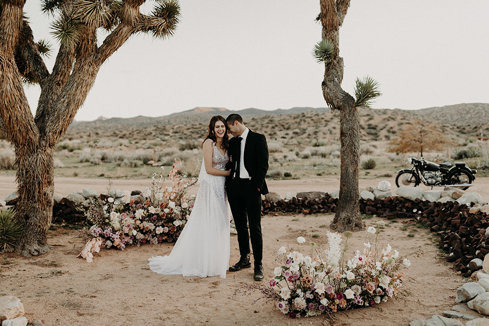 Rim-Rock-Ranch-Shoot-bride-and-groom-laughing-in-ceremony-space-bride-in-a-bohemian-style-dress-with-a-sheer-overlay-and-crown-groom-in-a-simple-black-suit-and-long-tie