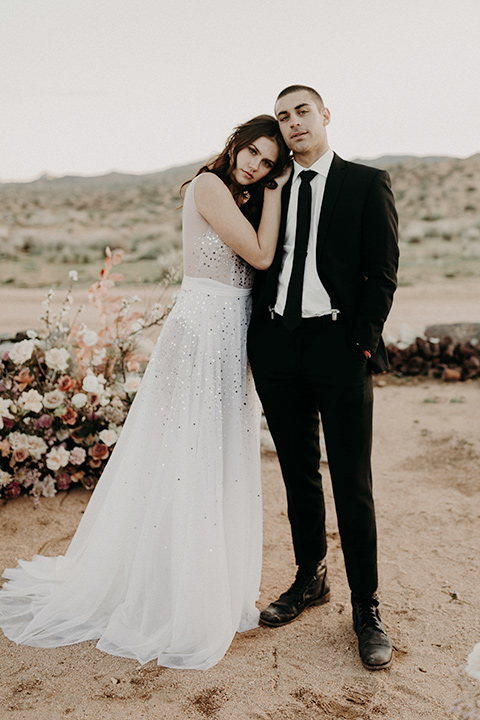 Rim-Rock-Ranch-Shoot-bride-resting-her-head-on-groom-bride-with-crown-on-and-a-sheer-bohemian-dress-with-crystals-and-flutter-sleeves-groom-in-a-white-shirt-black-pants-and-black-suspenders