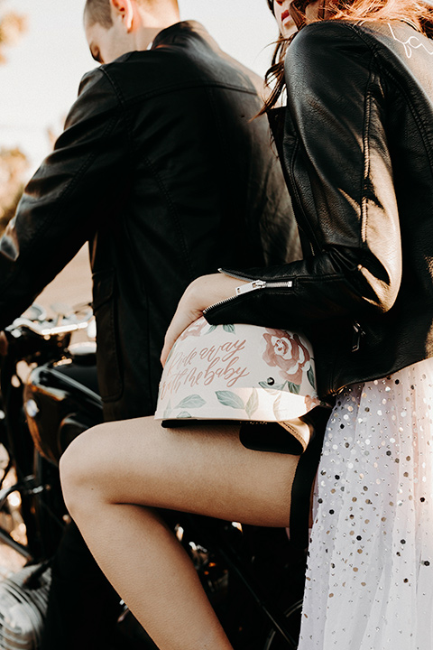 Rim-Rock-Ranch-Shoot-close-up-of-couple-on-bike-bride-with-crown-on-and-a-sheer-bohemian-dress-with-crsystals-and-flutter-sleeves-groom-in-a-white-shirt-black-pants-and-black-suspenders