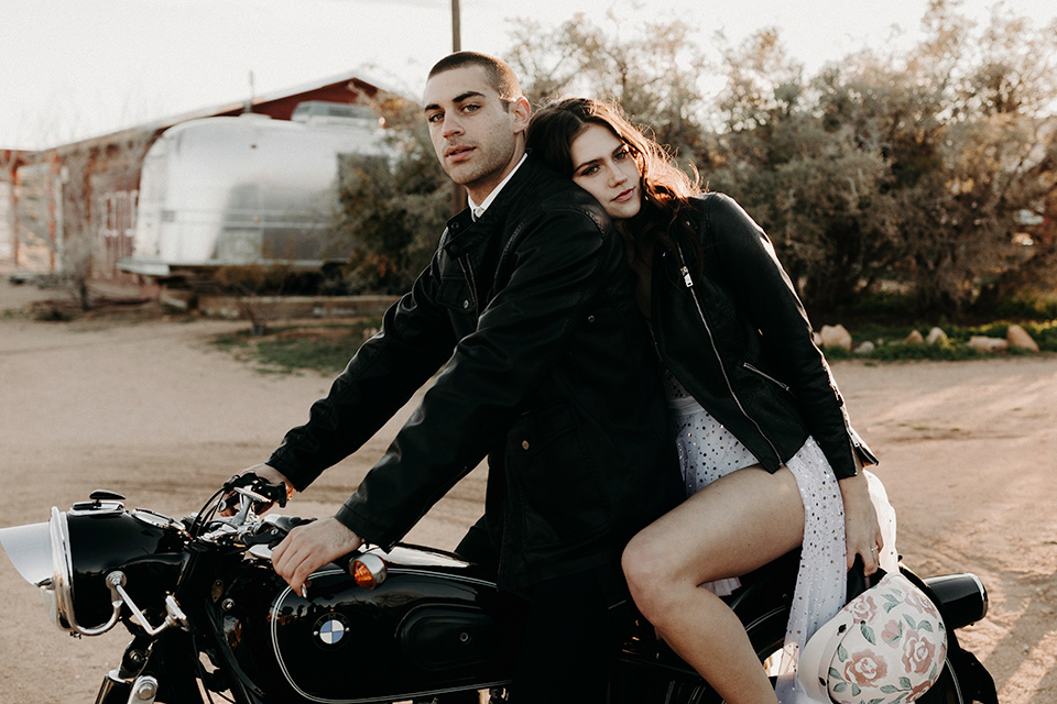 Rim-Rock-Ranch-Shoot-couple-on-motorcycle-bride-in-a-bohemian-style-dress-with-a-sheer-overlay-and-crown-groom-in-a-simple-black-suit-and-long-tie