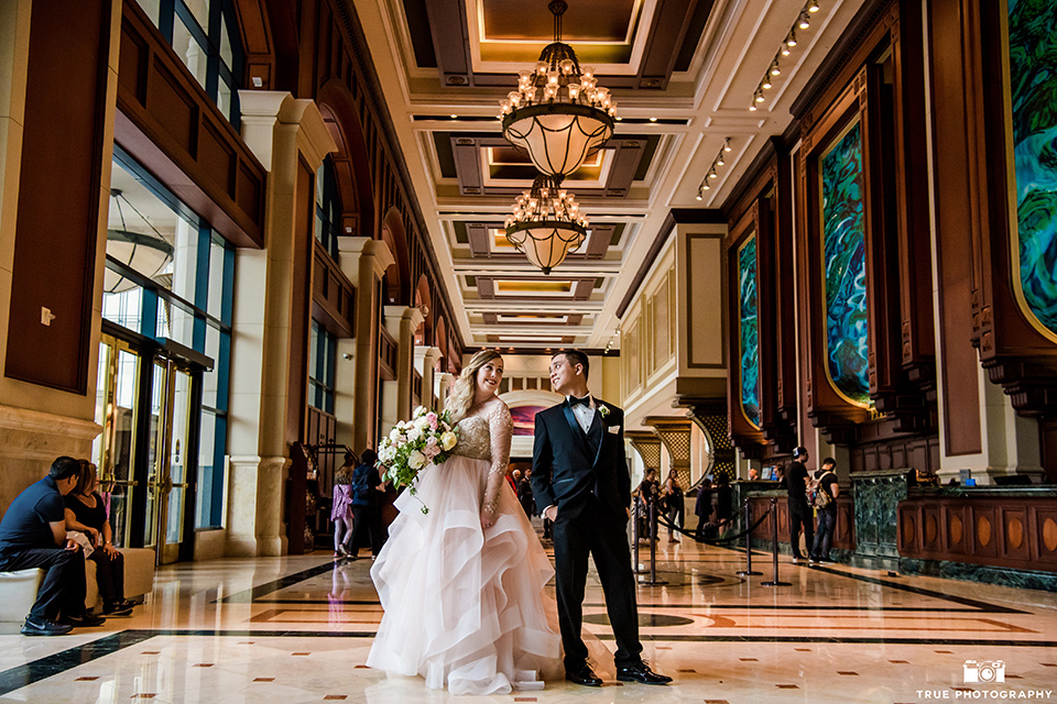 Hyatt-San-Diego-wedding-bride-and-groom-in-lobby-with-dogs-the-bride-is-in-a-blush-toned-ballgown-and-the-groom-in-a-black-shawl-lapel-tuxedo