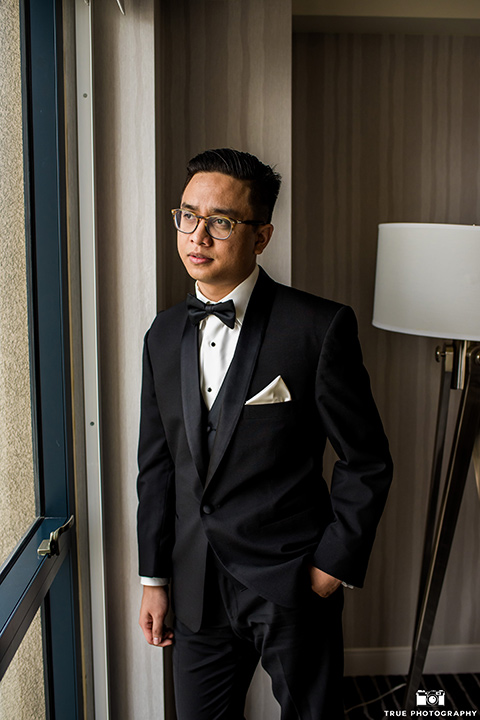 Hyatt-San-Diego-wedding-groom-looking-out-window-in-a-black-shawl-lape-tuxedo