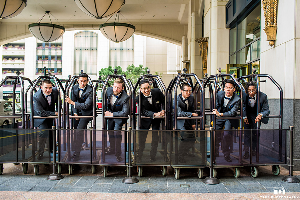 Hyatt-San-Diego-wedding-groomsmen-on-suitcase-carts-the-groom-in-a-black-shawl-lapel-tuxedo-the-groomsmen-in-grey-shalw-lapel-tuxedos