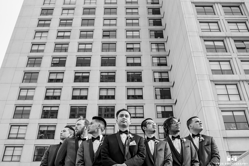 Hyatt-San-Diego-wedding-groomsmen-outside-venue-the-groom-in-a-black-shawl-lapel-tuxedo-the-groomsmen-in-grey-shalw-lapel-tuxedos