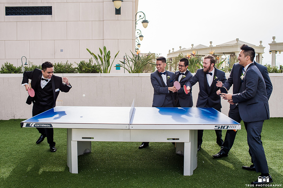 Hyatt-San-Diego-wedding-groomsmen-playing-ping-pong-the-groom-in-a-black-shawl-lapel-tuxedo-the-groomsmen-in-grey-shalw-lapel-tuxedos