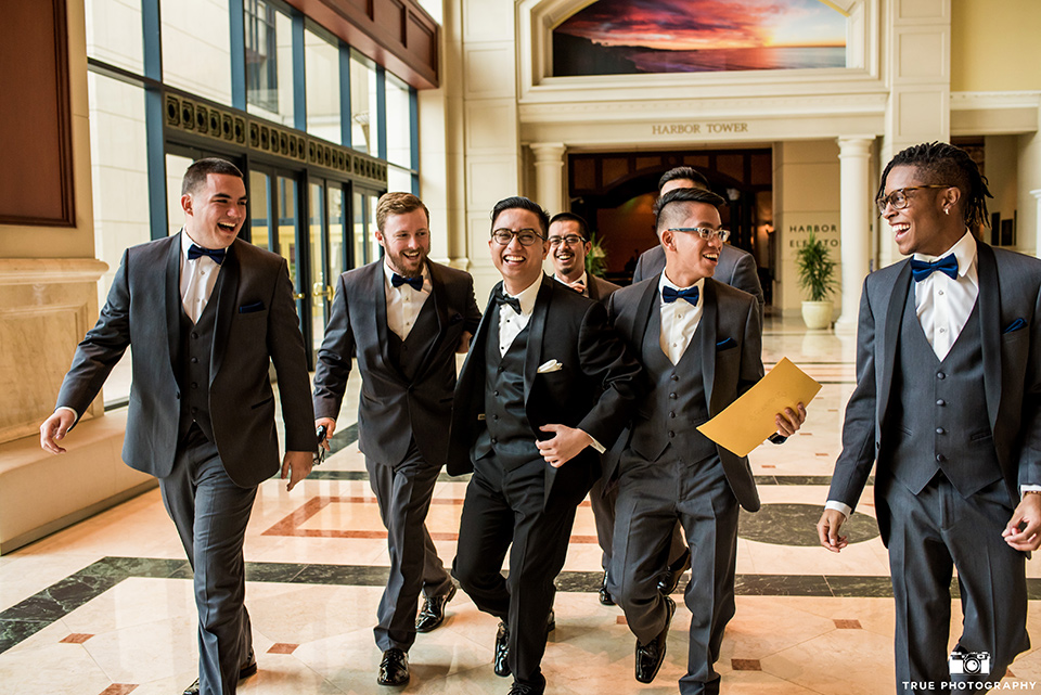 Hyatt-San-Diego-wedding-groomsmen-walking-in-lobby-the-groom-in-a-black-shawl-lapel-tuxedo-the-groomsmen-in-grey-shalw-lapel-tuxedos