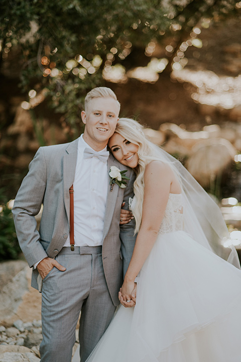 serendiity-gardens-bride-resting-her-head-on-groom-shoulder-bride-in-a-tulle-ballgown-with-straps-groom-in-a-grey-suit-with-brown-suspenders