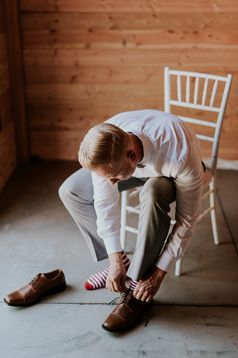 serendiity-gardens-groom-putting-on-shoes-groom-in-a-grey-suit-with-brown-suspenders