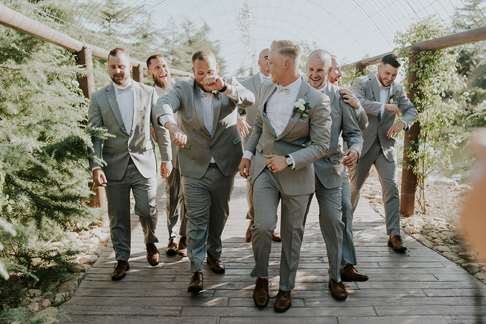 serendiity-gardens-groomsmen-walking-all-in-grey-suits-with-brown-suspenders