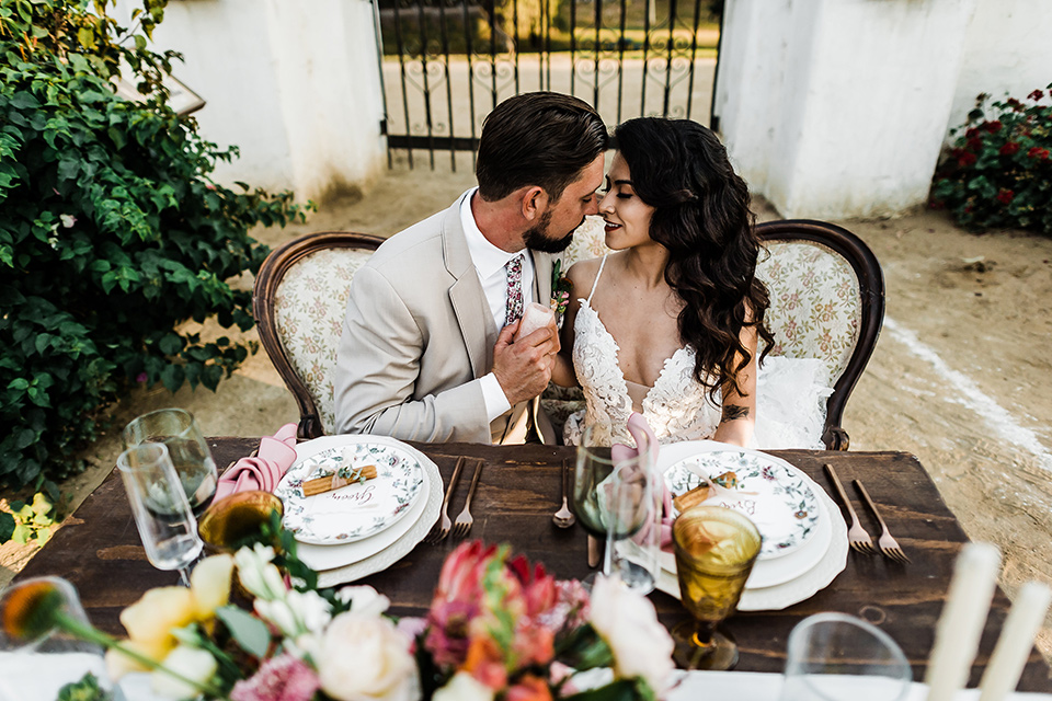 Olivas-Adobe-spanish-inspired-shoot-bride-and-groom-at-sweetheart-table-bride-in-a-spanish-inspired-lace-dress-and-groom-in-a-tan-suit