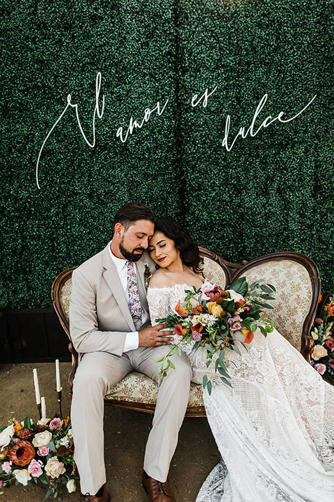 Olivas-Adobe-spanish-inspired-shoot-bride-resting-on-groom-bride-wearing-a-lace-gown-with-sleeves-and-holding-a-large-bouquet-of-flowers-groom-wearing-a-tan-suit-with-a-floral-tie