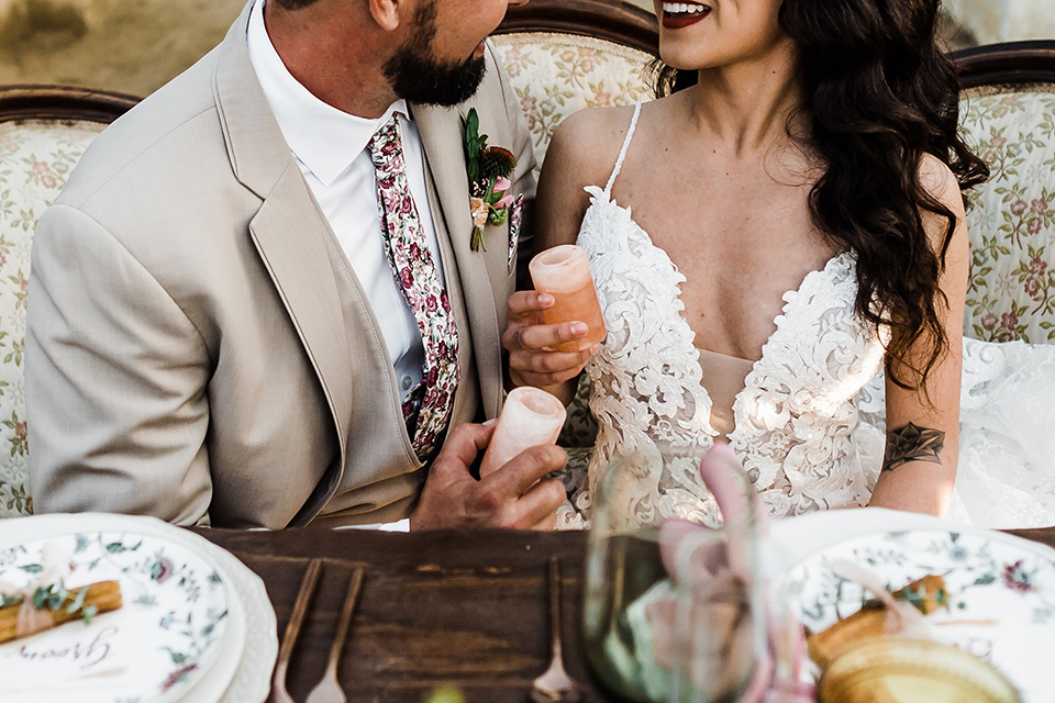 Olivas-Adobe-spanish-inspired-shoot-close-up-on-coule-at-sweetheart-table-bride-in-a-spanish-inspired-lace-dress-with-long-sleeves-and-groom-in-a-tan-suit-with-a-floral-tie