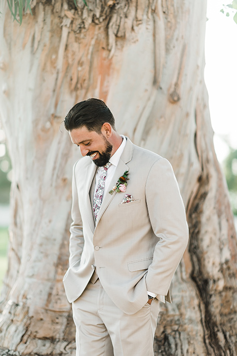 Olivas-Adobe-spanish-inspired-shoot-groom-looking-down-wearing-a-tan-suit-with-a-white-floral-neck-tie