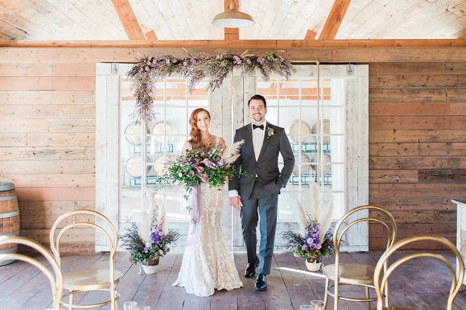 triunfo-creek-vineyards-wedding-bride-and-groom-walking-away-from-ceremony-bride-in-a-lace-gown-in-a-blush-tone-groom-in-a-grey-tuxedo-with-a-black-bow-tie