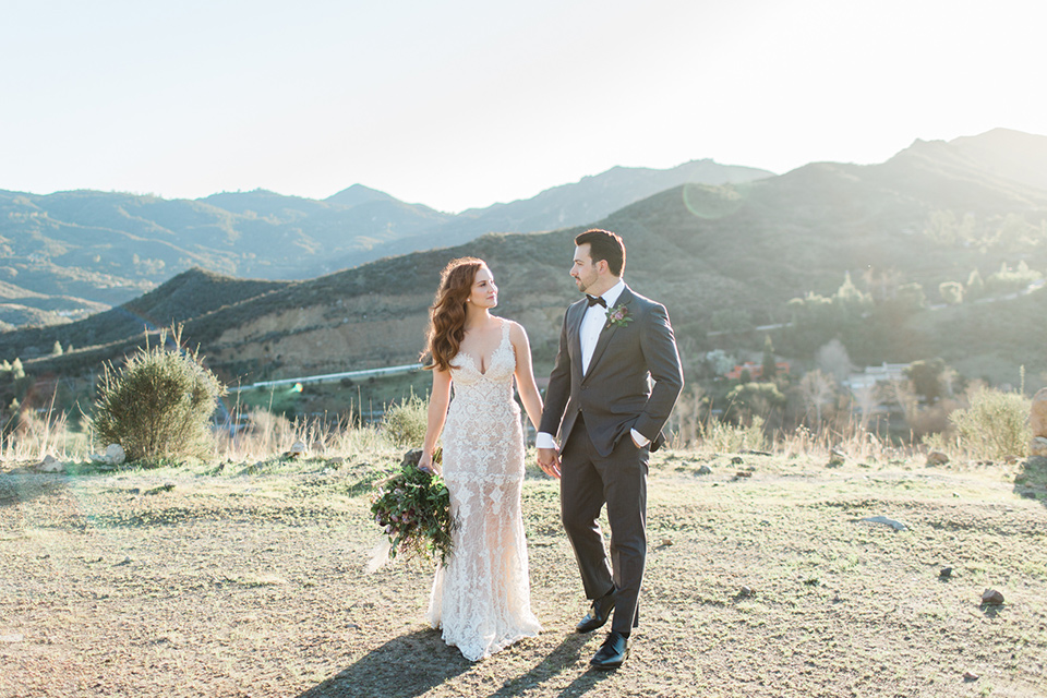 triunfo-creek-vineyards-wedding-bride-and-groom-walking-away-bride-in-a-lace-gown-in-a-blush-tone-groom-in-a-grey-tuxedo-with-a-black-bow-tie