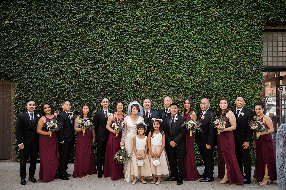 villa-del-sol-wedding-bridal-party-bridesmaids-in-burgundy-dresses-groomsmen-in-black-shawl-lapel-tuxedos-bride-in-a-spanish-inspired-lace-gown-with-a-deep-v-and-long-sleeves-groom-in-a-navy-shawl-lapel-tuxedo-with-a-burgundy-tie