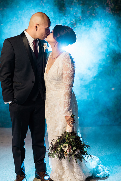 villa-del-sol-wedding-bride-and-groom-with-fog-behind-them-bride-in-a-spanish-inspired-lace-gown-with-sleeves-groom-in-a-navy-shawl-lapel-tuxedo-with-a-burgundy-tie