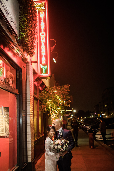 villa-del-sol-wedding-bride-and-groom-with-neon-signs-bride-in-a-lace-gown-with-long-sleeves-groom-in-a-navy-shawl-lapel-tuxedo-with-a-burgundy-tie