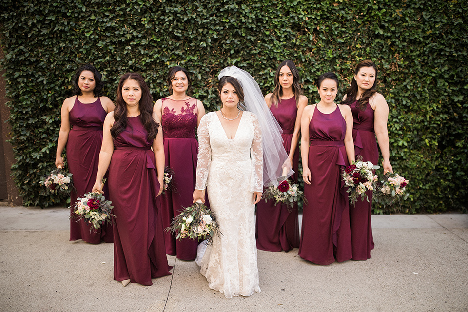 villa-del-sol-wedding-bridesmaids-bride-in-a-spanish-inspired-lace-gown-with-a-deep-v-and-long-sleeves-bridesmaids-in-deep-burgundy-dresses