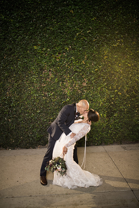 villa-del-sol-wedding-groom-dipping-bride-bride-in-a-lace-gown-with-long-sleeves-groom-in-a-navy-shawl-lapel-tuxedo-with-a-burgundy-tie