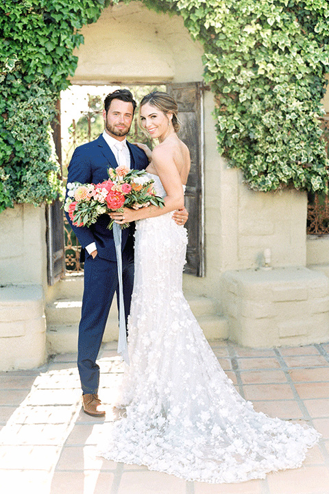 whispering-rose-shoot-bride-and-groom-smiling-at-the-camera-bride-wearing-a-strapless-gown-with-pink-shoes-groom-in-a-cobalt-blue-suit-with-brown-shoes-and-an-ivory-tie